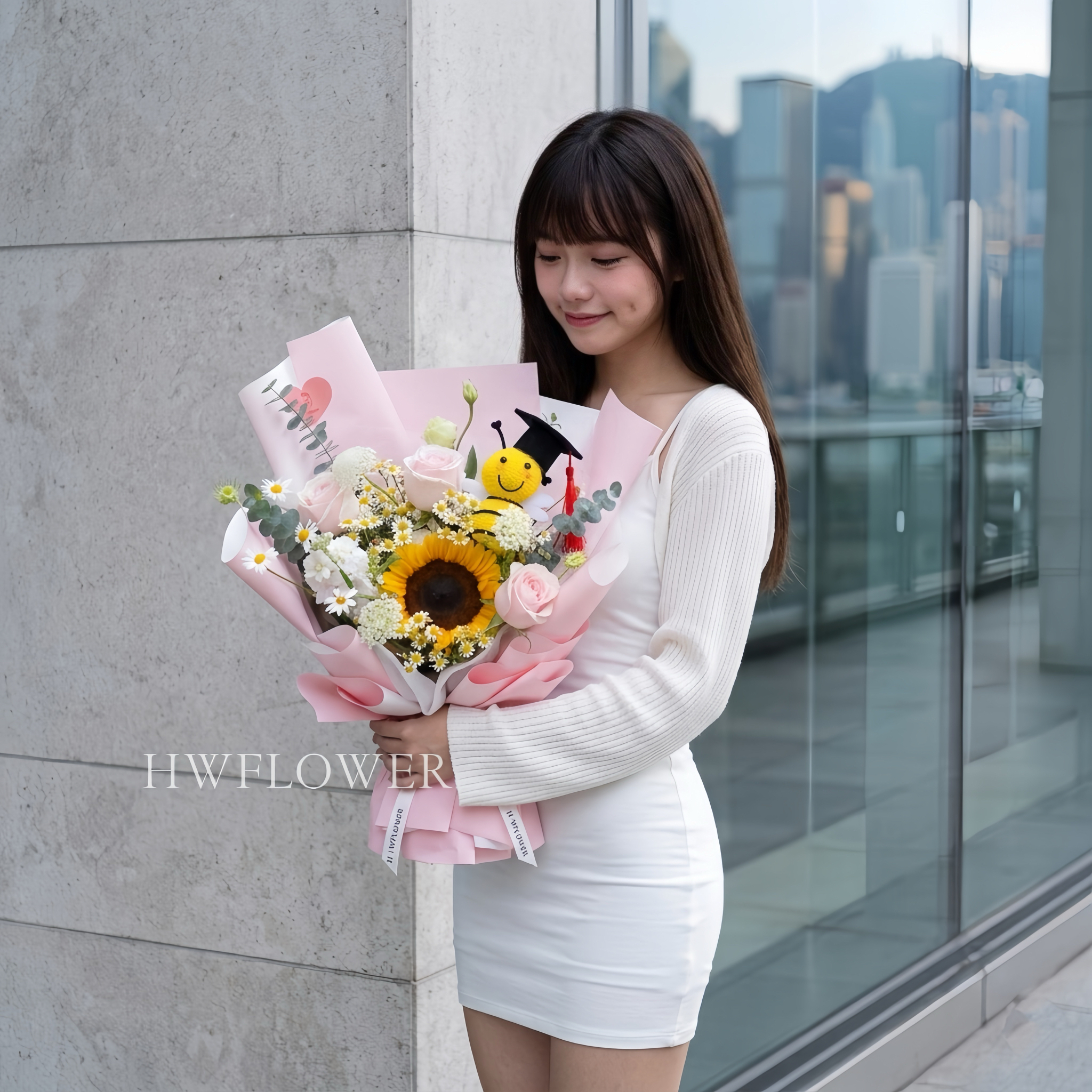 A woman holding a pink graduation bouquet with a sunflower, pink roses, white daisies, and a graduation bee plush.