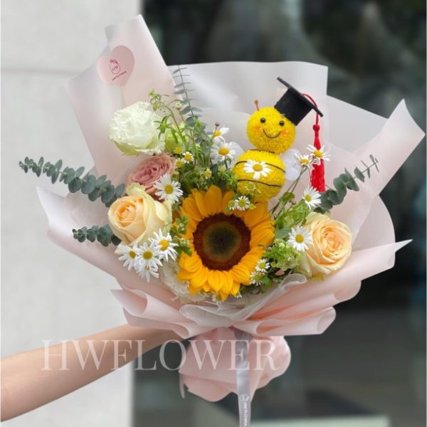 向日葵畢業花束配畢業公仔及香檳玫瑰,小雛菊點綴粉色包裝,適合幼稚園、小學及畢業典禮送禮的鮮花花束。