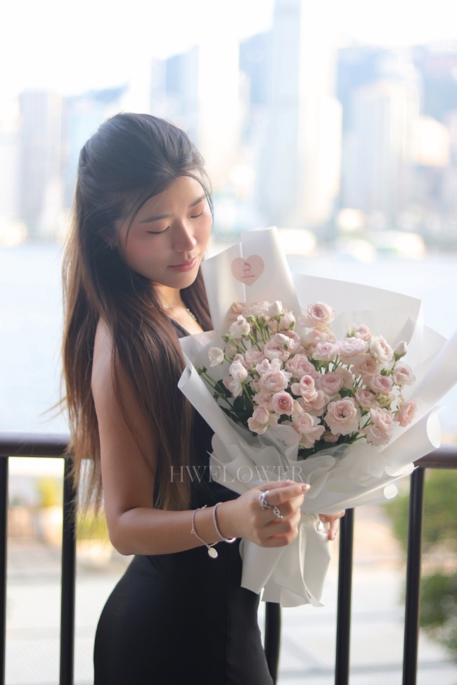 Woman holding a light pink spray rose bouquet with white wrapping