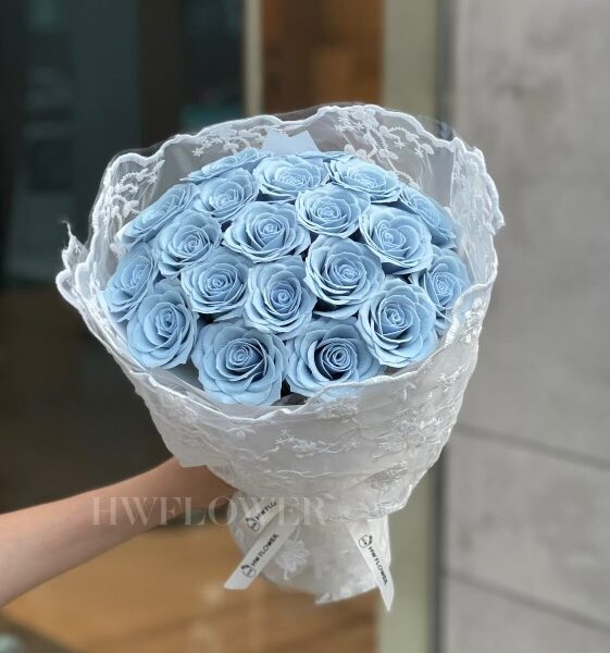 A woman holding a dusty blue soap rose bouquet with delicate lace wrapping, showcasing its elegant design.