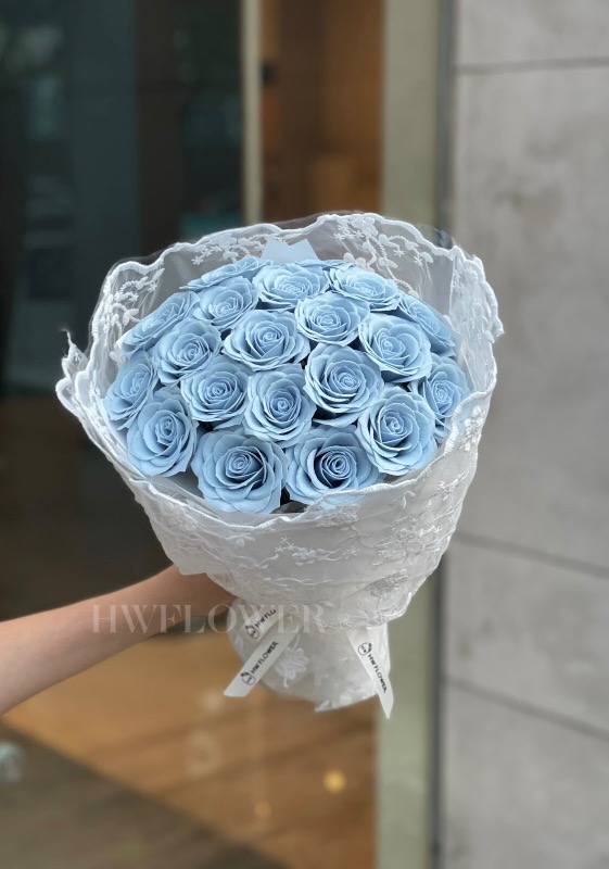 A woman holding a dusty blue soap rose bouquet with delicate lace wrapping, showcasing its elegant design.